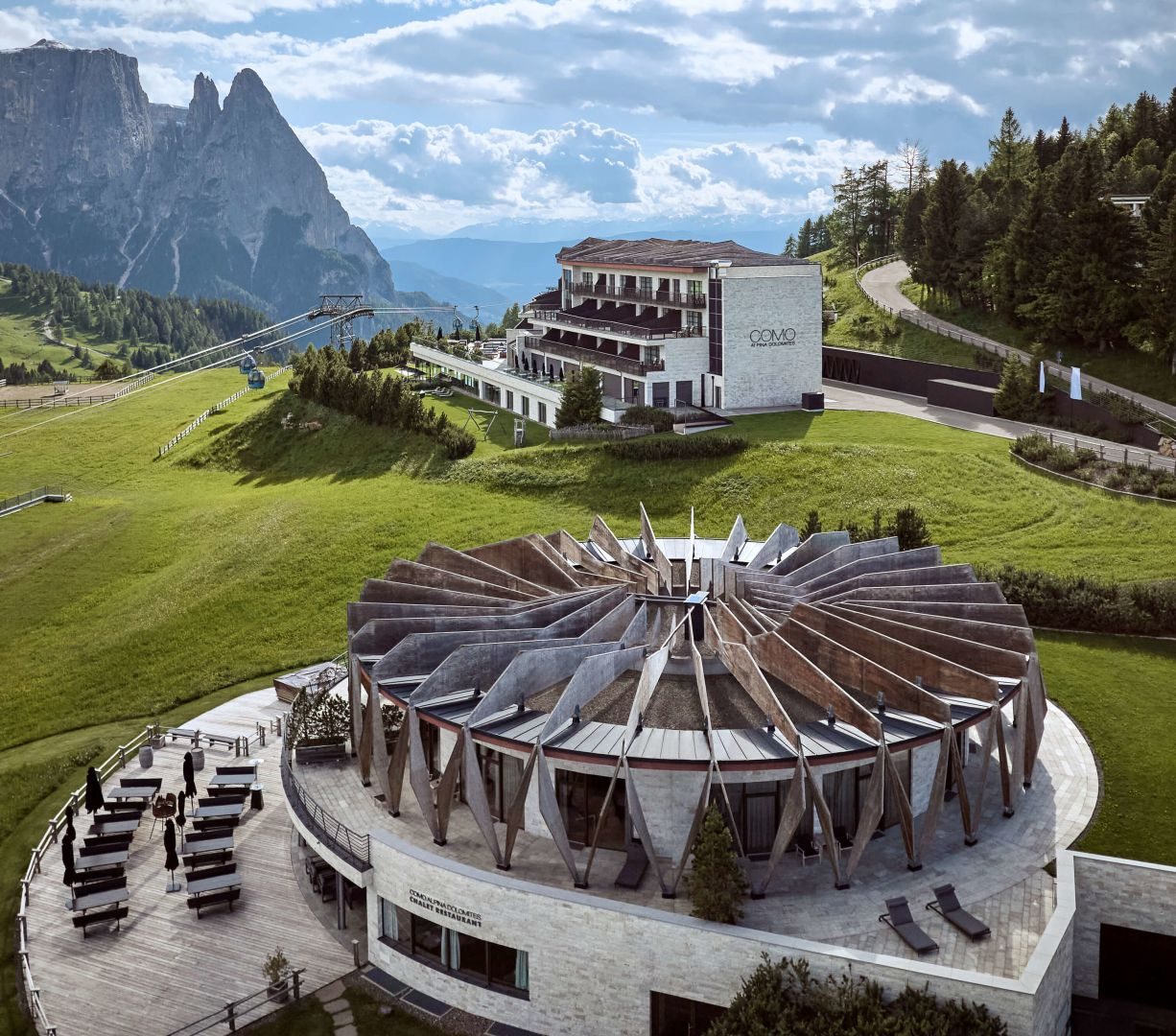COMO Alpina Dolomites and its round Chalet Restaurant on the Alpe di Siusi, with the Sciliar behind and a lift running past the hotel