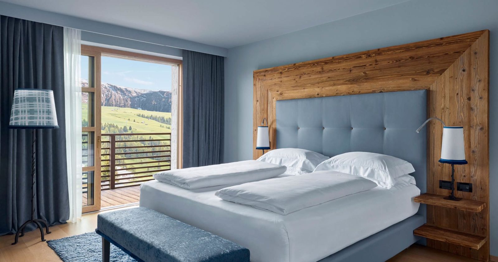 A COMO Alpina room with a reclaimed-wood headboard and a balcony over the meadows