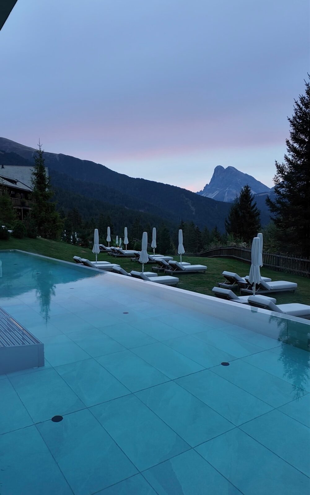 The Forestis outdoor pool at dusk, with loungers on the lawn and the peaks beyond