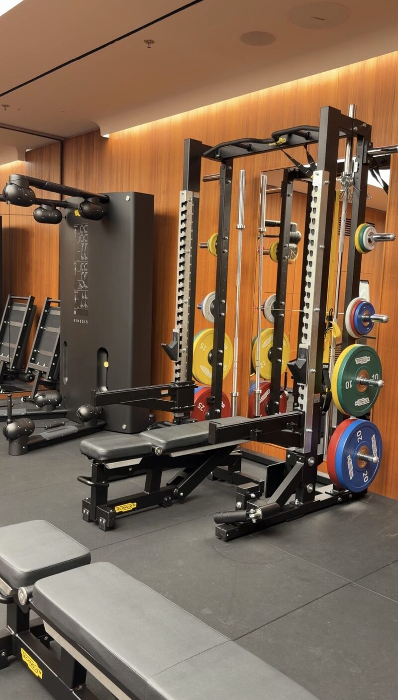 The Bulgari Hotel Roma gym, with Technogym racks, benches and plates against warm wood paneling