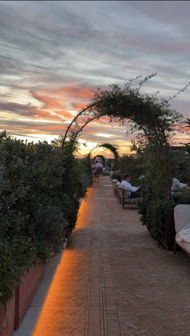 The Bulgari Hotel Roma rooftop at sunset, a herringbone brick walkway under green arches lined with lounge seating