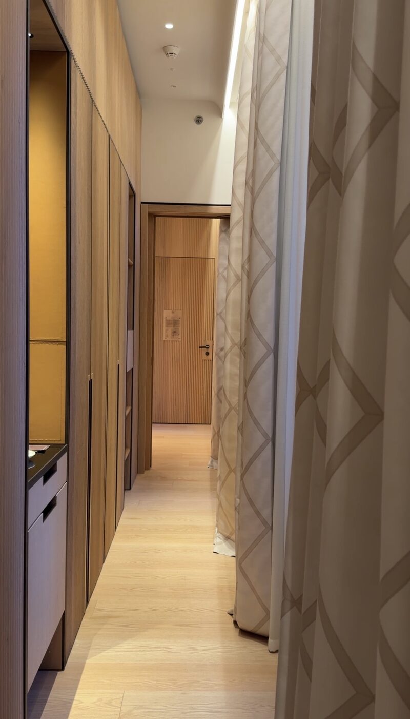 The entry hall of a Bulgari Hotel Roma room, with wood-paneled wardrobes, an oak floor and patterned curtains