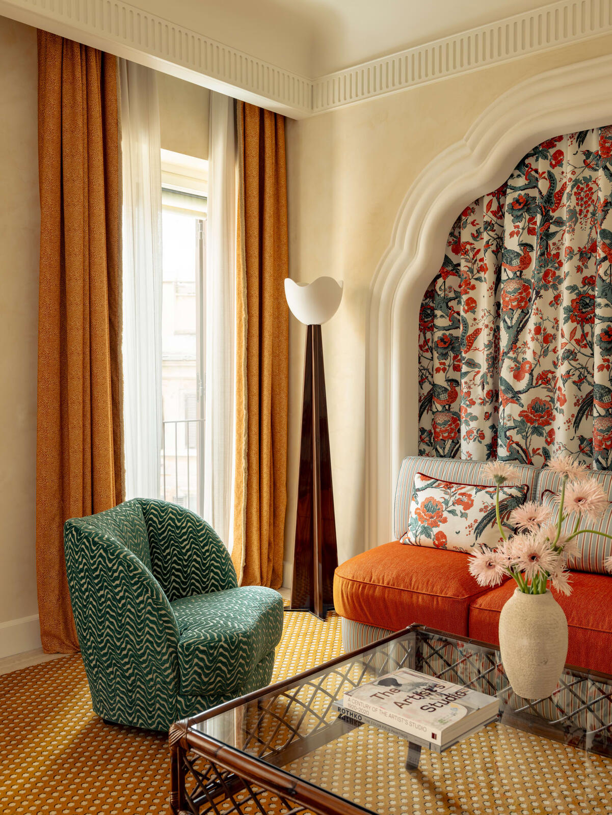 A Casa Monti room with orange curtains, a green zigzag armchair, a tulip floor lamp and a bird-print fabric alcove
