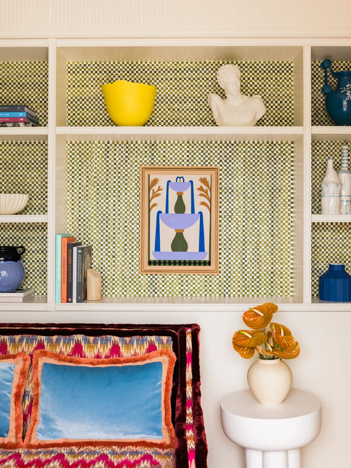 Casa Monti shelves backed in green checkerboard tile, with ceramics, a classical bust and a colorful print above a flame-stitch sofa