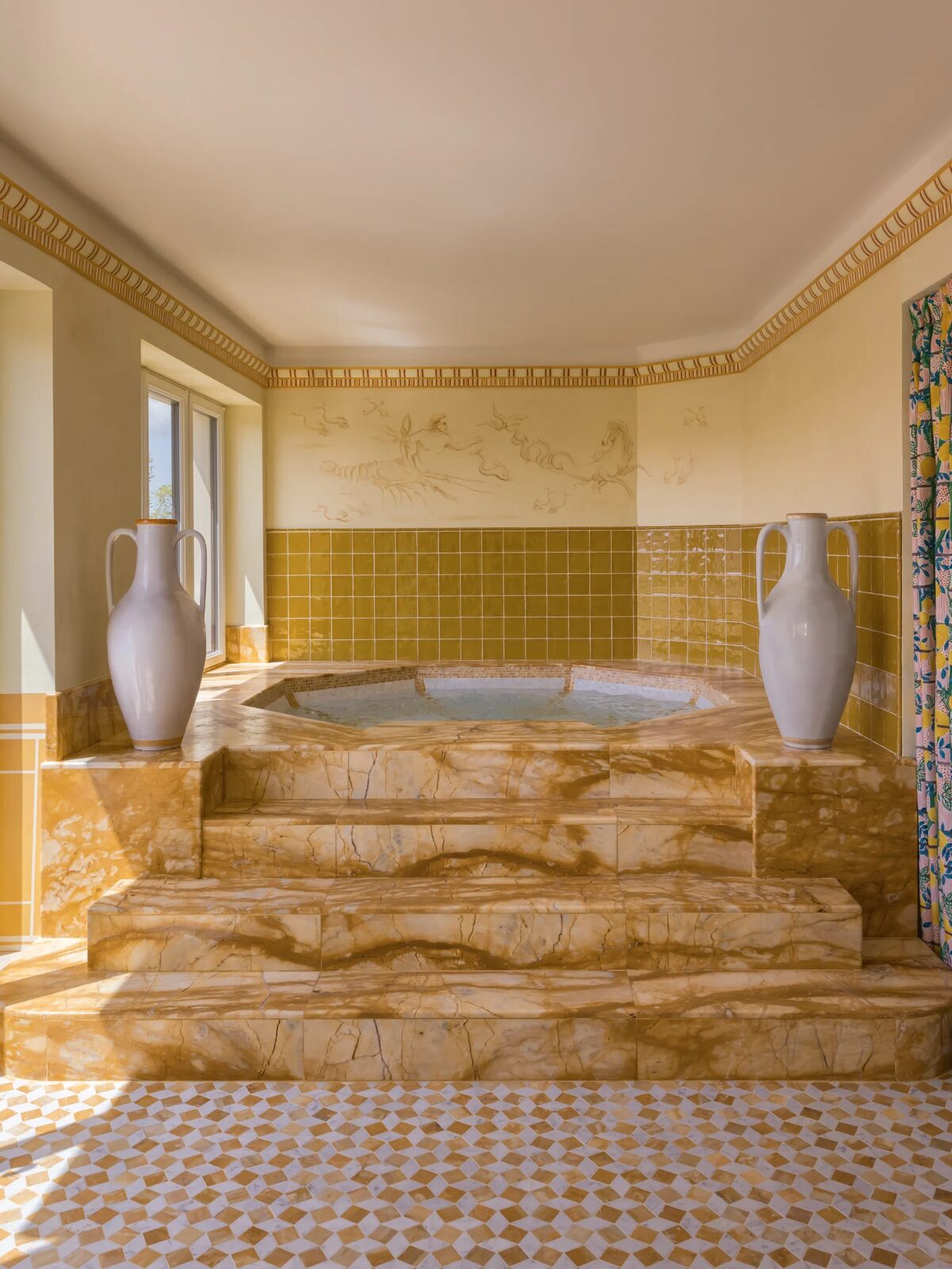 The Casa Monti spa pool, raised on golden marble steps between two white amphorae, with yellow tiles and a painted frieze