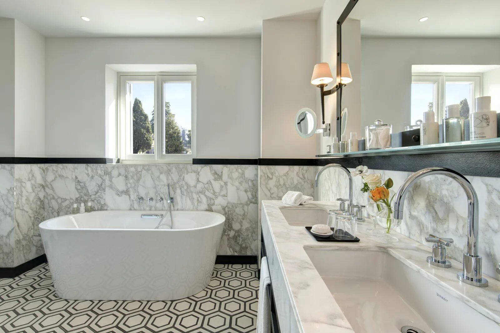 A Hotel de la Ville bathroom with a freestanding tub, marble walls, a hexagon tile floor and a double vanity