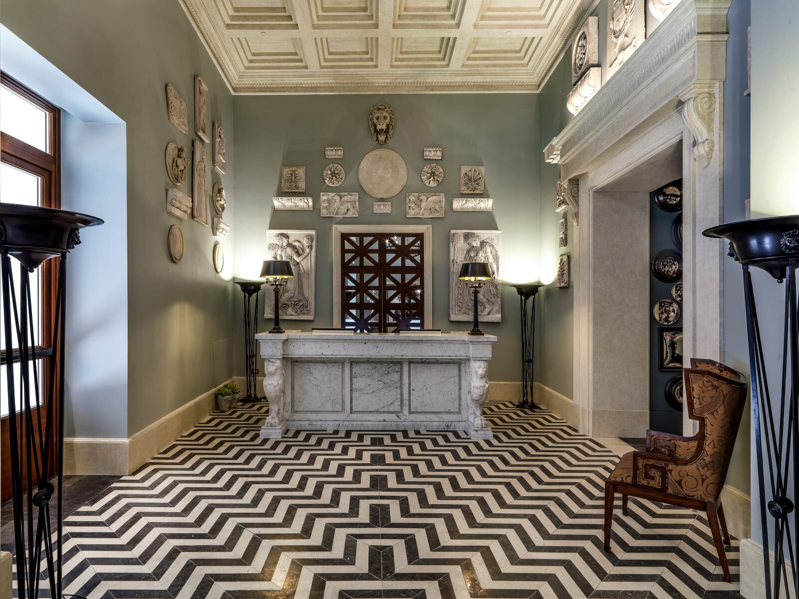 Hotel de la Ville’s reception, with a marble desk, plaster reliefs on sage walls and a black and white zigzag floor