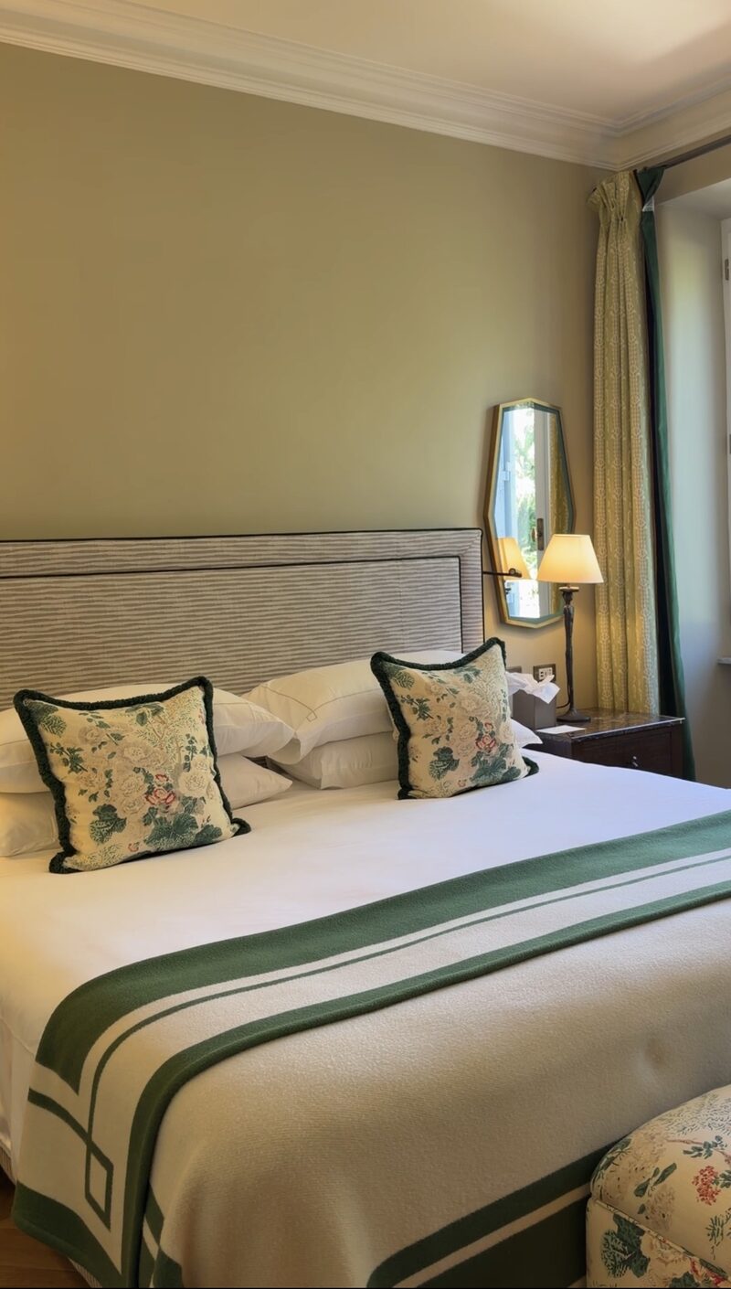 A renovated Hotel de Russie bedroom in soft green, with a striped headboard, floral cushions and a green-banded throw