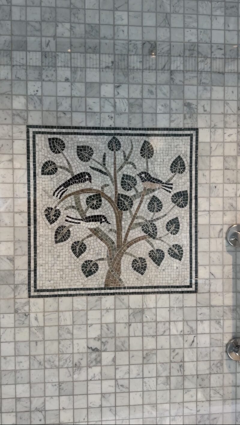 A stone mosaic of birds in a leafy tree set into the marble tiles of a Hotel de Russie shower