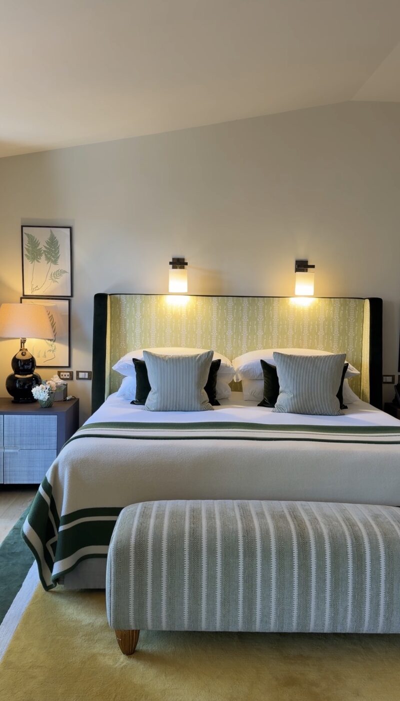 A Hotel de Russie suite bedroom with a green patterned headboard, botanical prints and a striped bench
