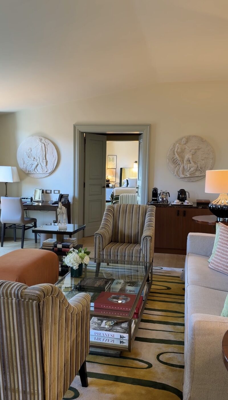 A Hotel de Russie suite living room with striped armchairs, a sofa, classical plaster roundels and a door through to the bedroom