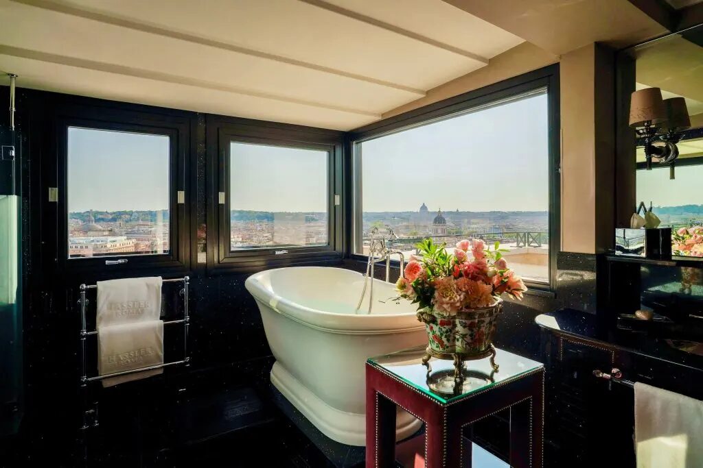 A freestanding tub in a black marble Hotel Hassler Roma bathroom, with windows over the rooftops to St. Peter’s
