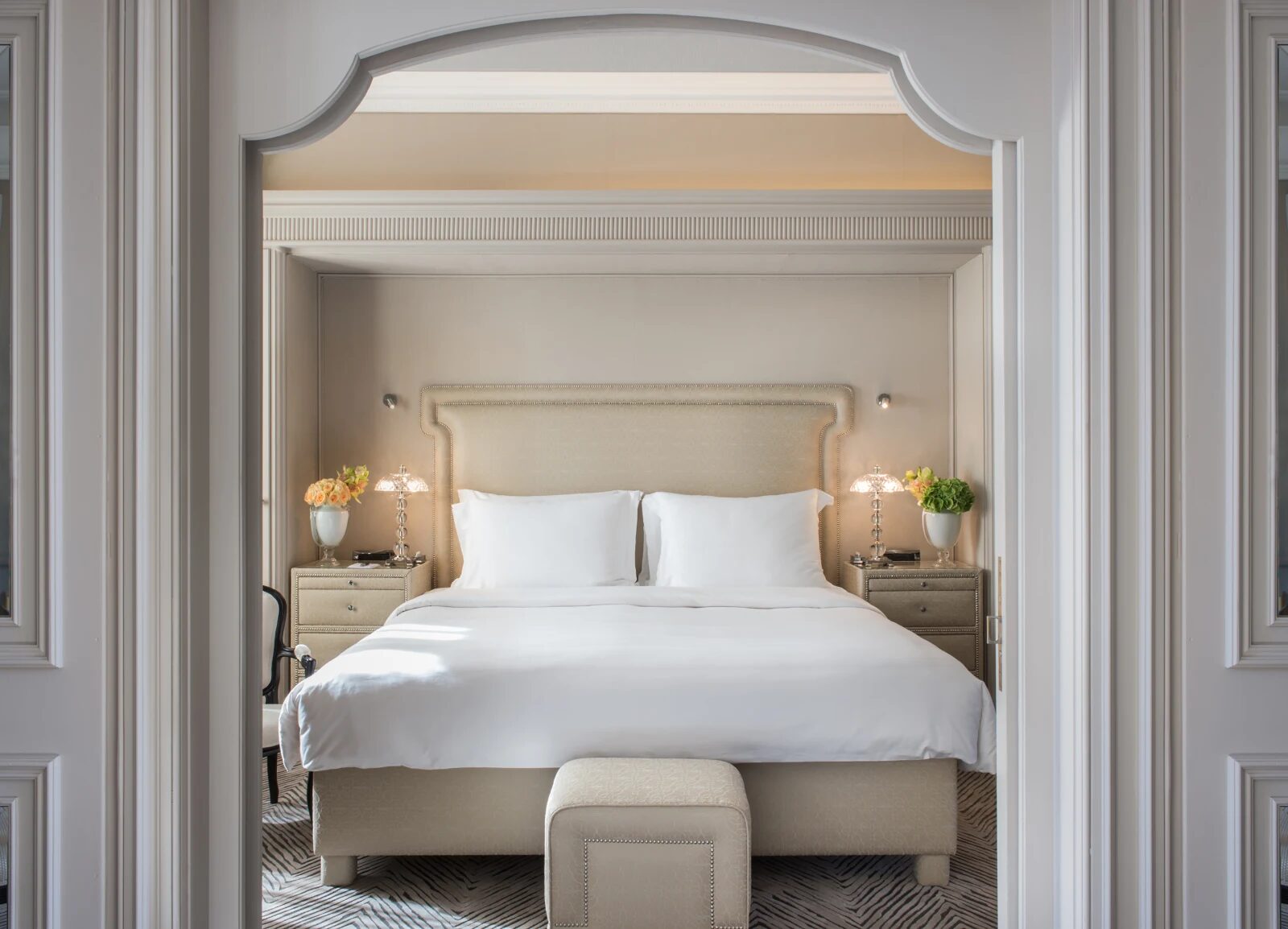 A Hotel Hassler Roma bedroom framed by an arched doorway, with a studded headboard and crystal lamps