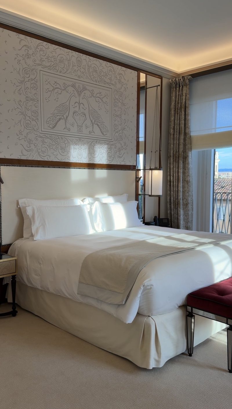 A bright Hotel Eden bedroom with a peacock relief above the bed and a balcony over the rooftops