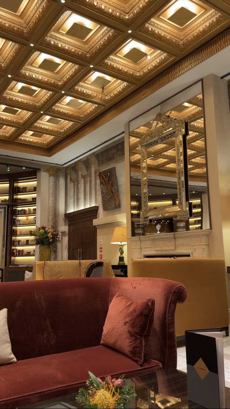 Hotel Eden&rsquo;s lobby lounge with a gilded coffered ceiling, velvet sofas and bookshelves