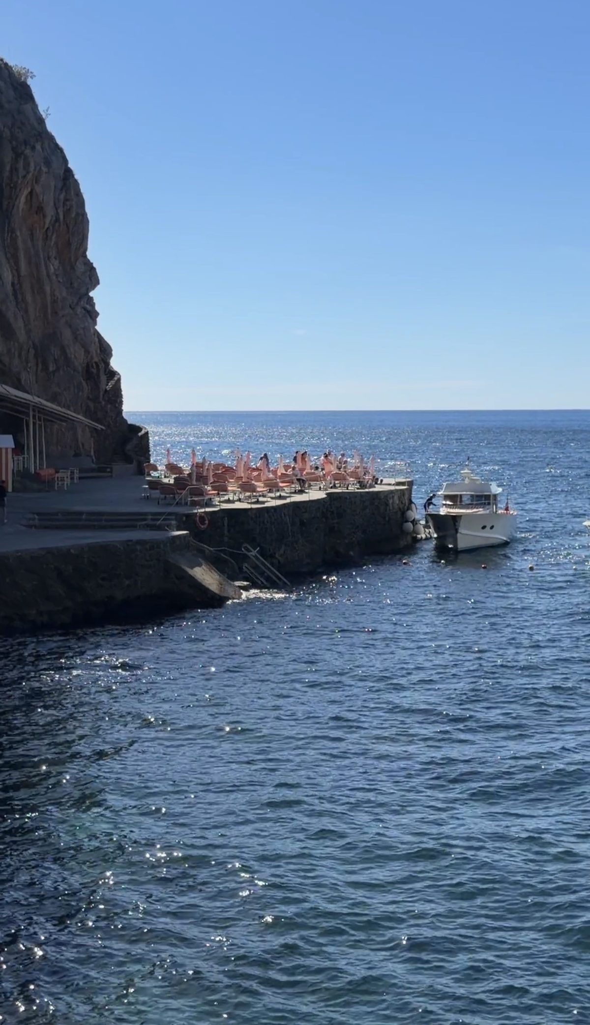 The Il San Pietro beach club on a rock platform at the foot of the cliff, with a boat alongside