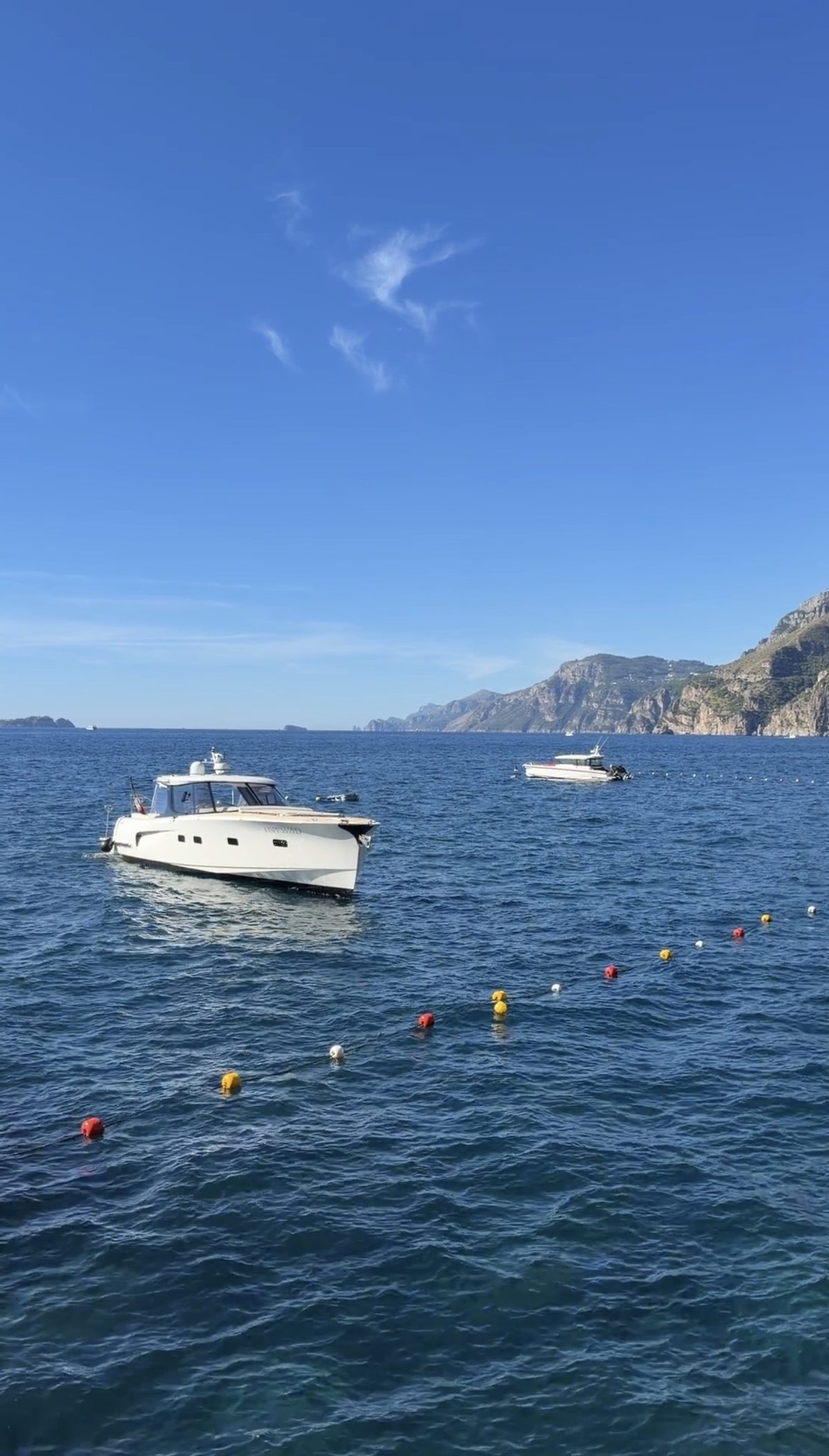 A white motor yacht moored off the Amalfi Coast near Il San Pietro, with the cliffs beyond
