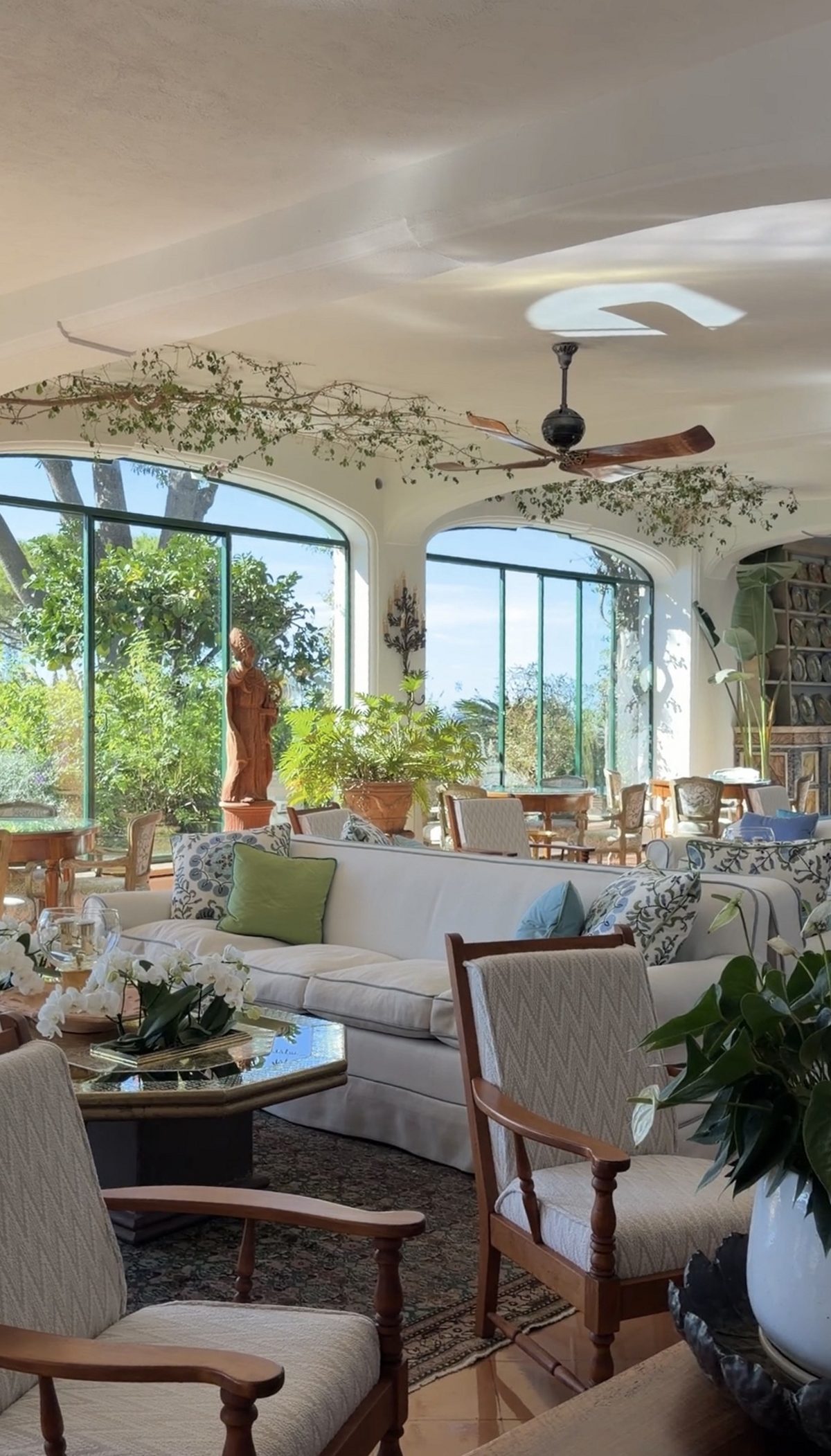 A bright lounge at Il San Pietro with white sofas, vines across the ceiling and arched windows onto the garden