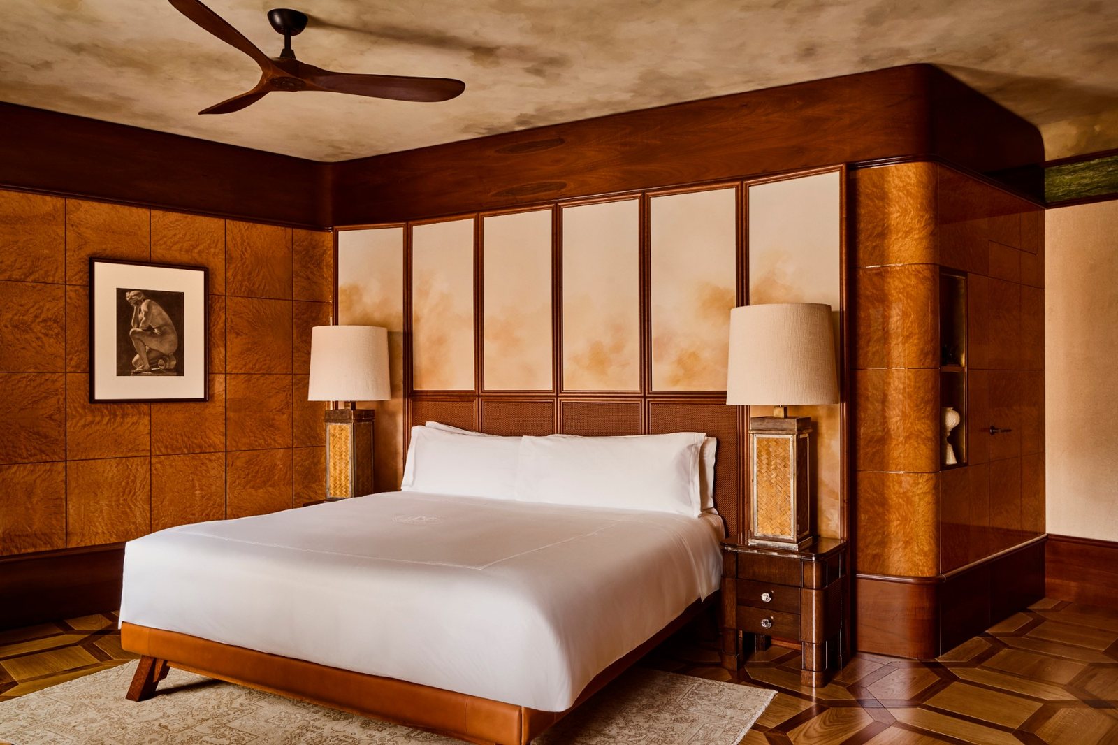 A bedroom at La Minerva with burl wood paneling, a leather bed frame and linen lamps