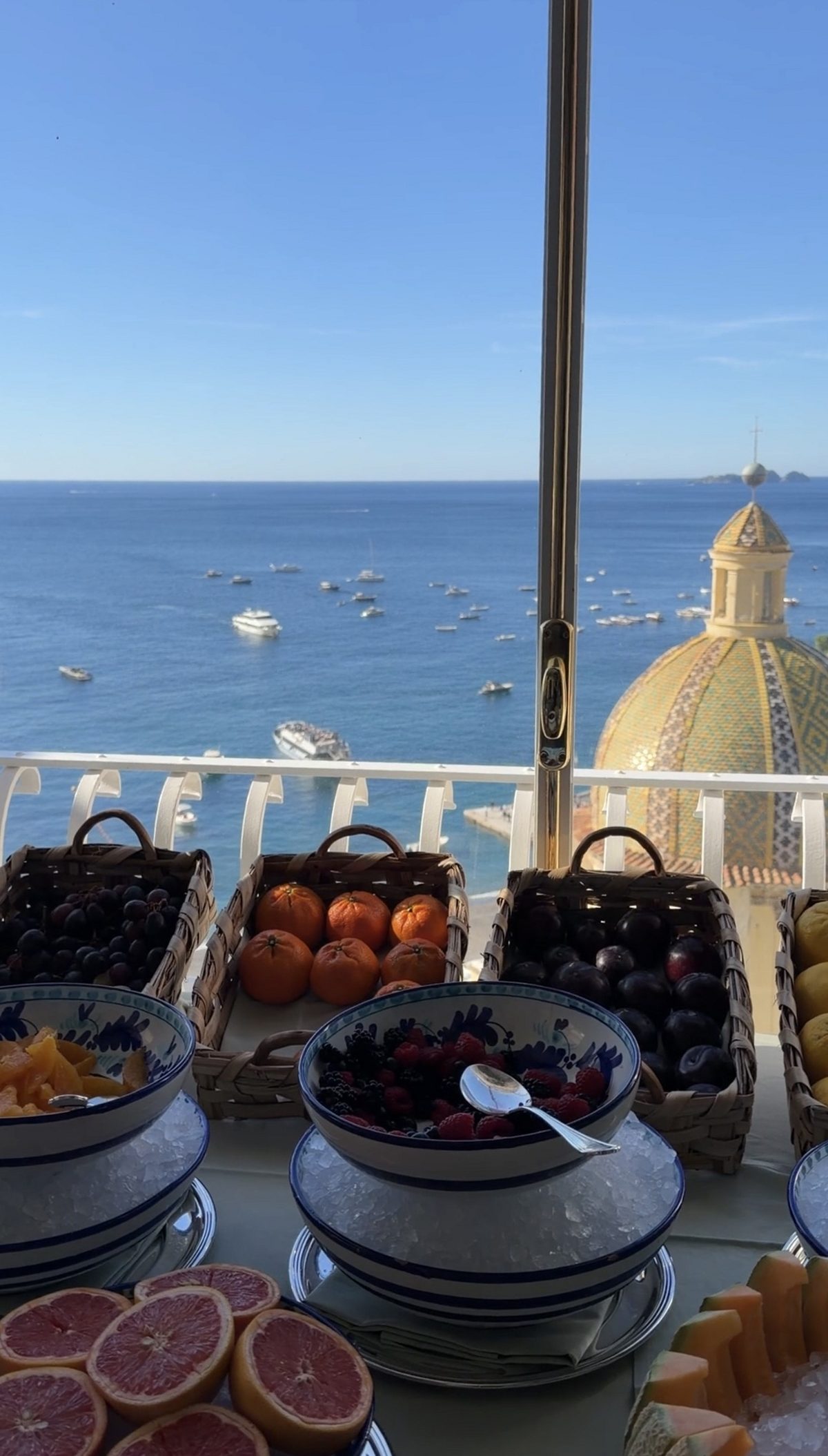 Fruit in hand-painted bowls on ice at the Le Sirenuse breakfast, with the church dome and the bay beyond
