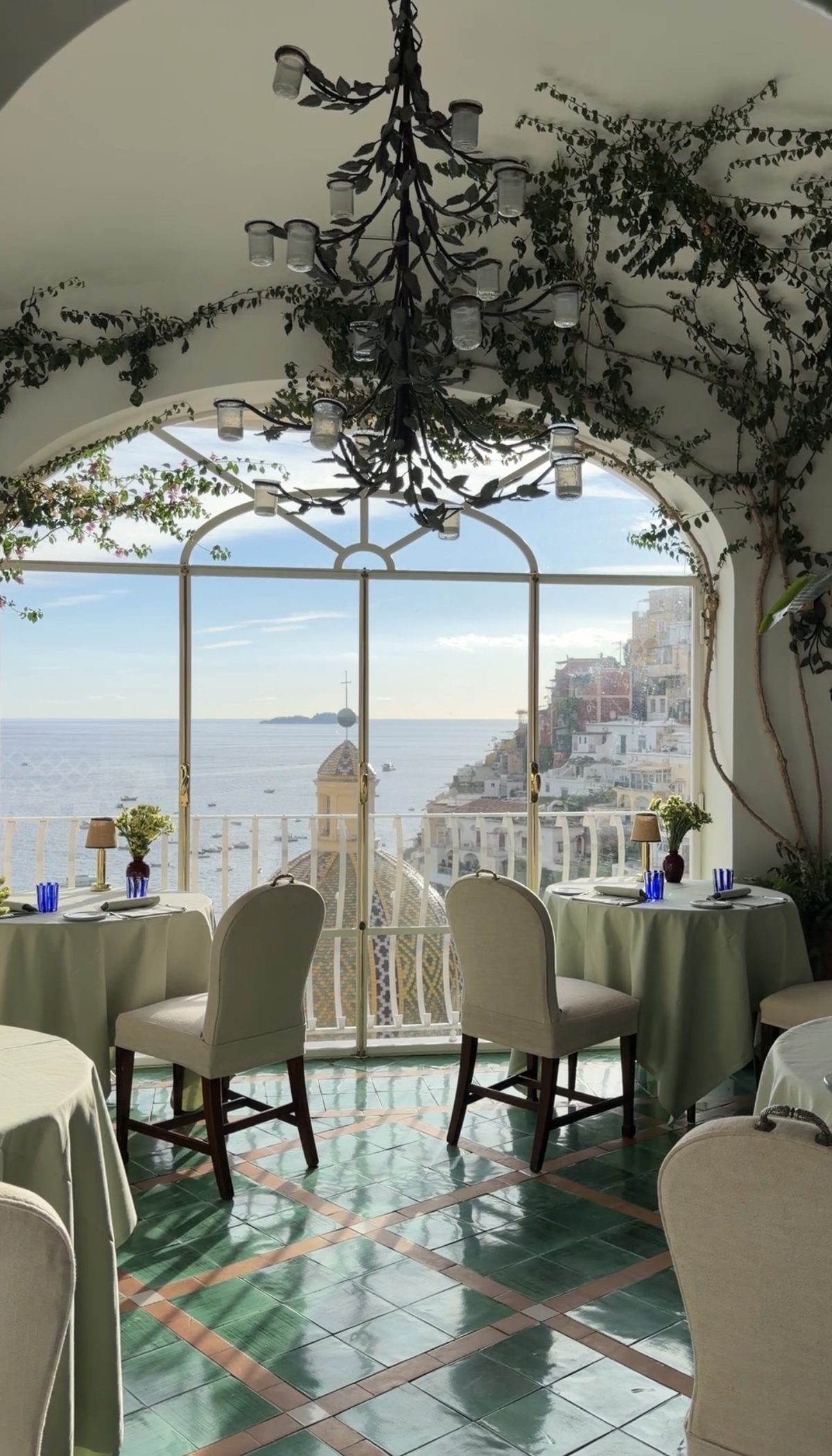 A table by an arched window in the Le Sirenuse dining room, looking over the church dome to the sea and Positano