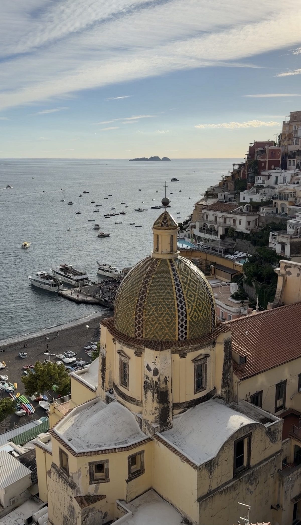 The tiled dome of Santa Maria Assunta from above, with the beach, the ferry pier and Li Galli on the horizon