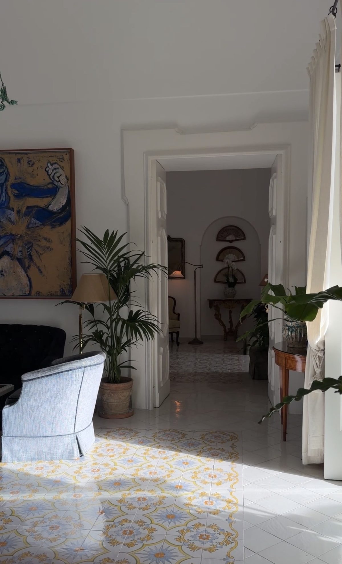 A sunlit Le Sirenuse lounge with a large painting, palms and hand-painted majolica tiles