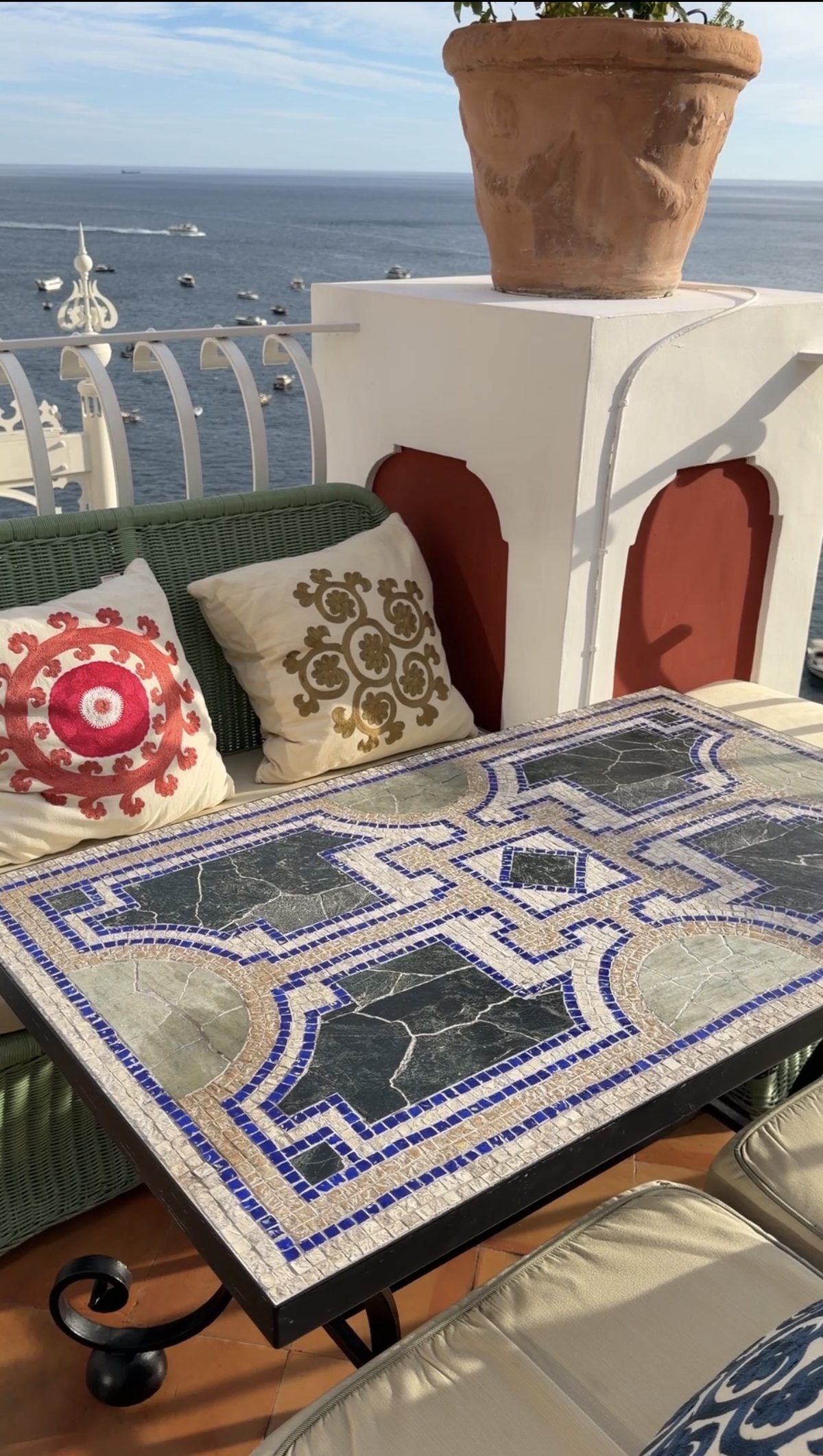 A mosaic table and embroidered cushions on a Le Sirenuse terrace above the boats in the bay