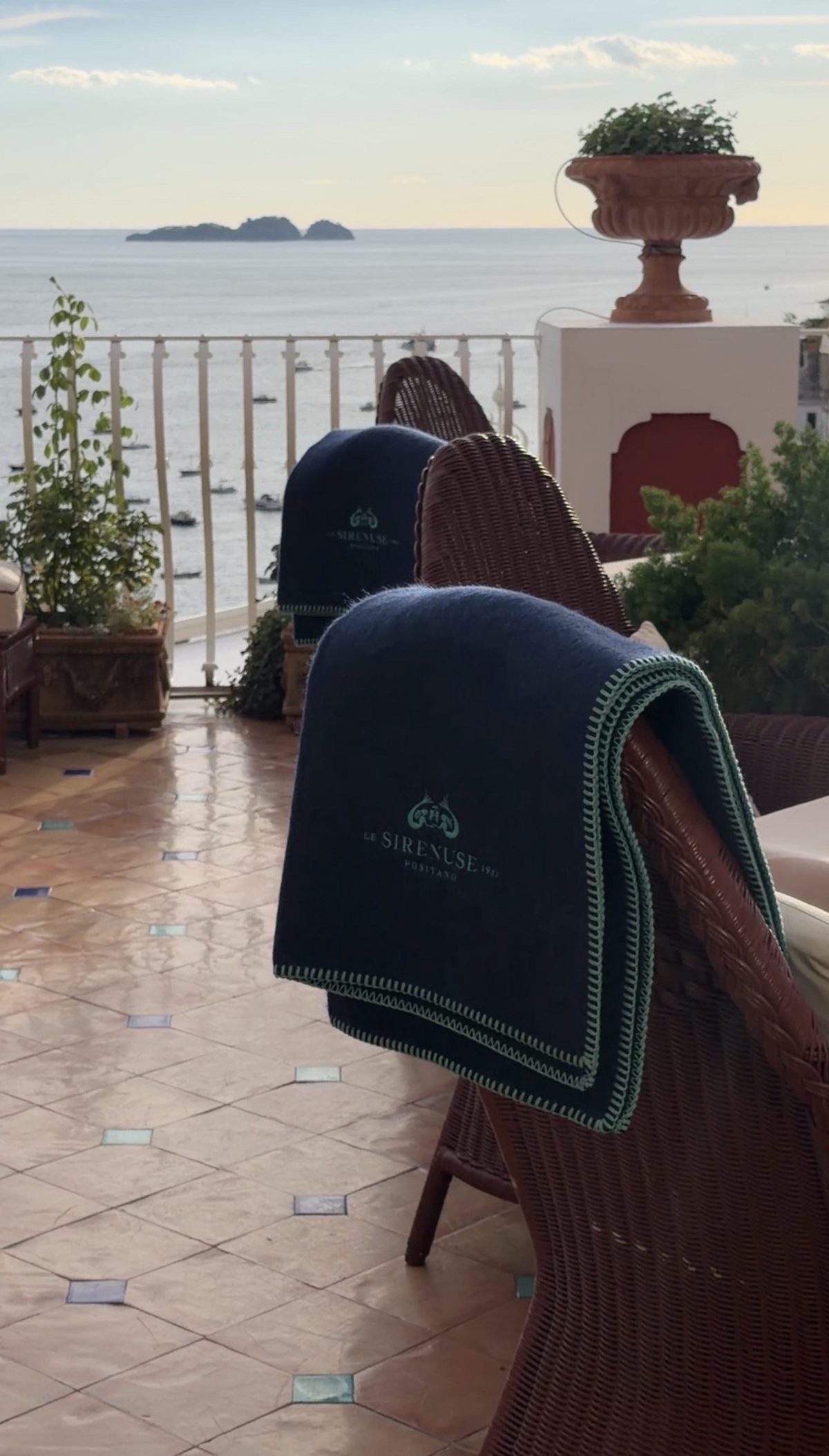 Navy Le Sirenuse blankets on wicker chairs on the terrace at dusk, with Li Galli on the horizon