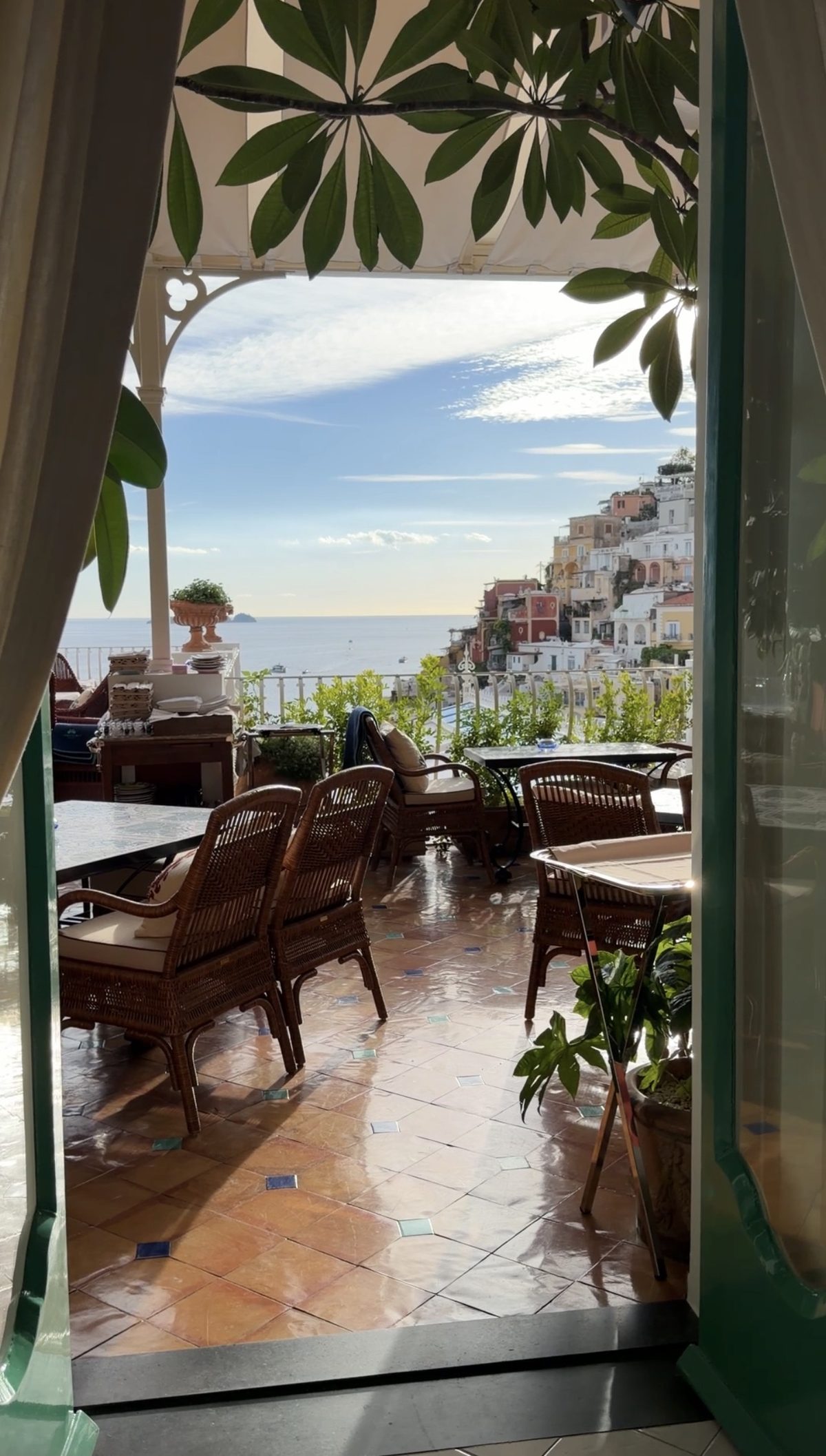 Through a green doorway to a terrace of wicker chairs at Le Sirenuse, with the houses of Positano and the sea beyond