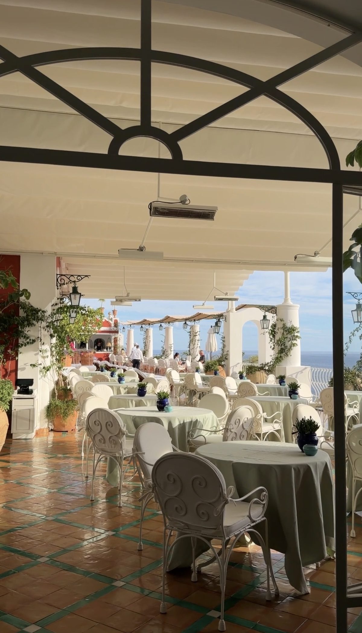 The covered terrace restaurant at Le Sirenuse with white wrought-iron chairs, columns and the sea beyond