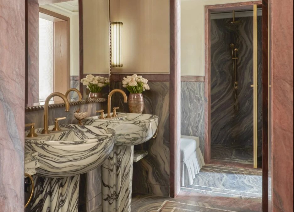 A bathroom in book-matched marble with brass taps and a marble shower