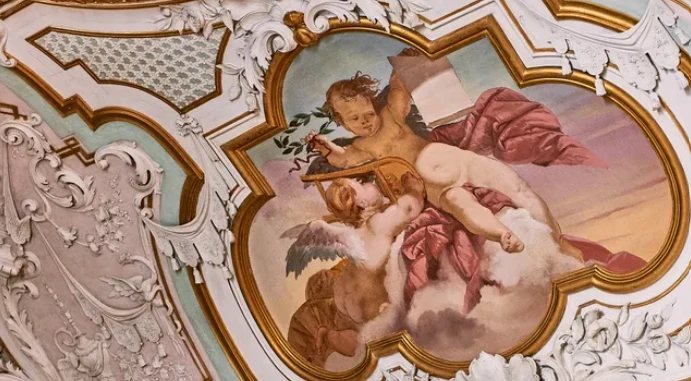 A restored ceiling fresco of cherubs framed in gilded stucco