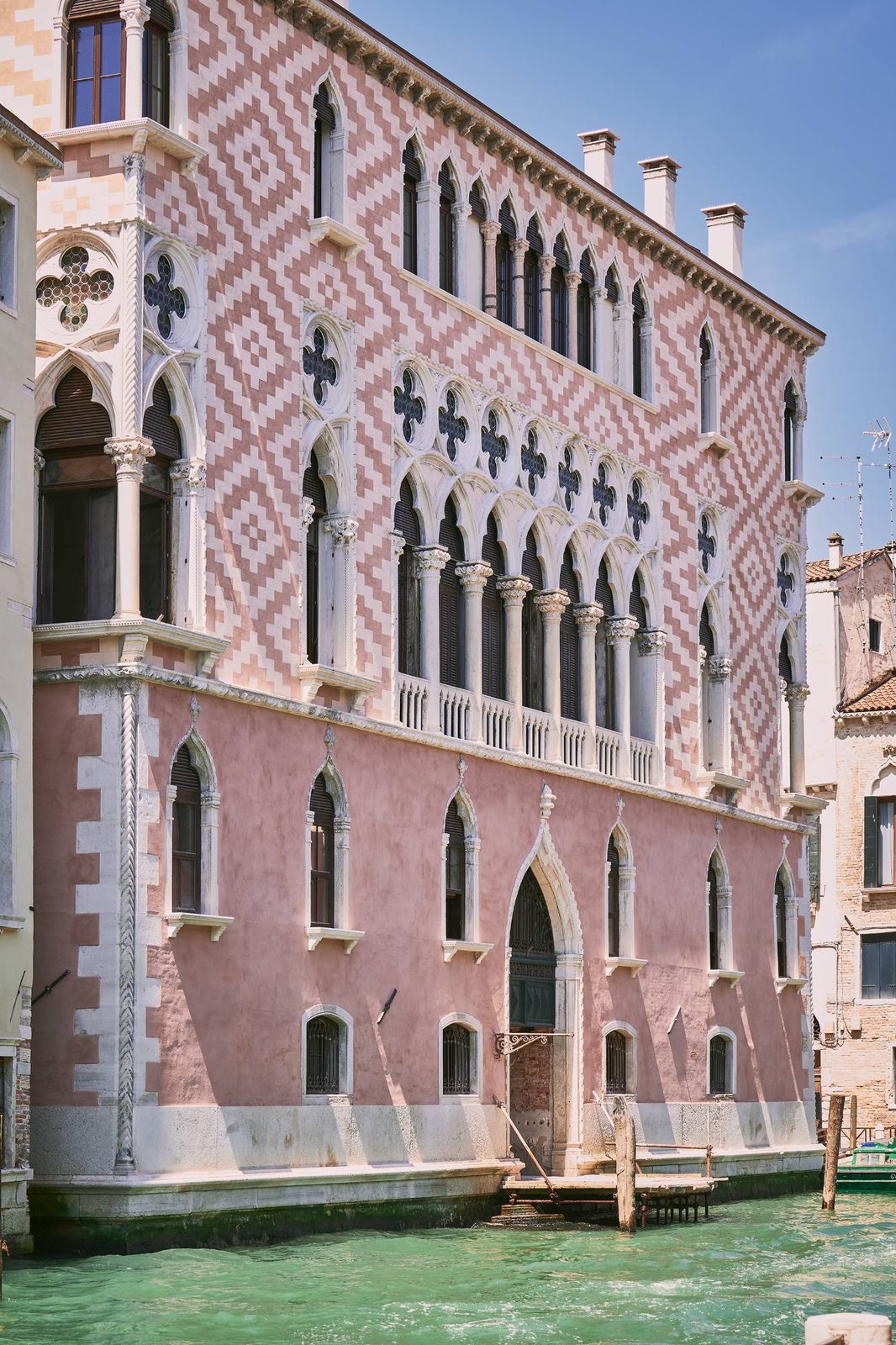 The pink and white diamond-patterned Gothic facade of Orient Express Venice on the water