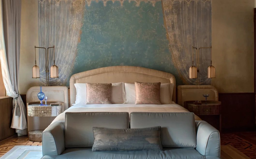 A bedroom with a painted fresco of blue drapery behind the bed