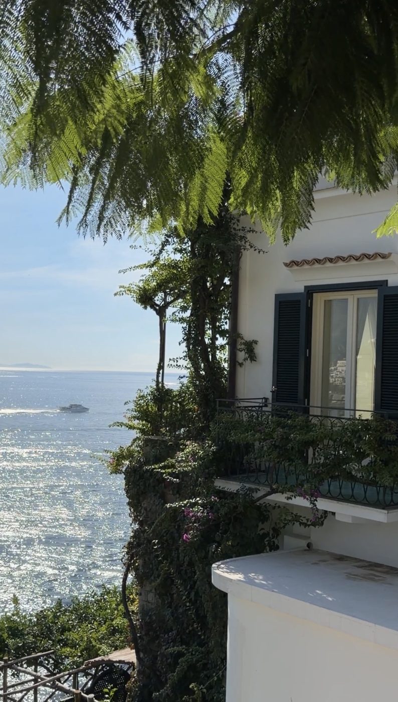 A white villa with dark shutters and a bougainvillea-covered balcony above the sea at Hotel Santa Caterina