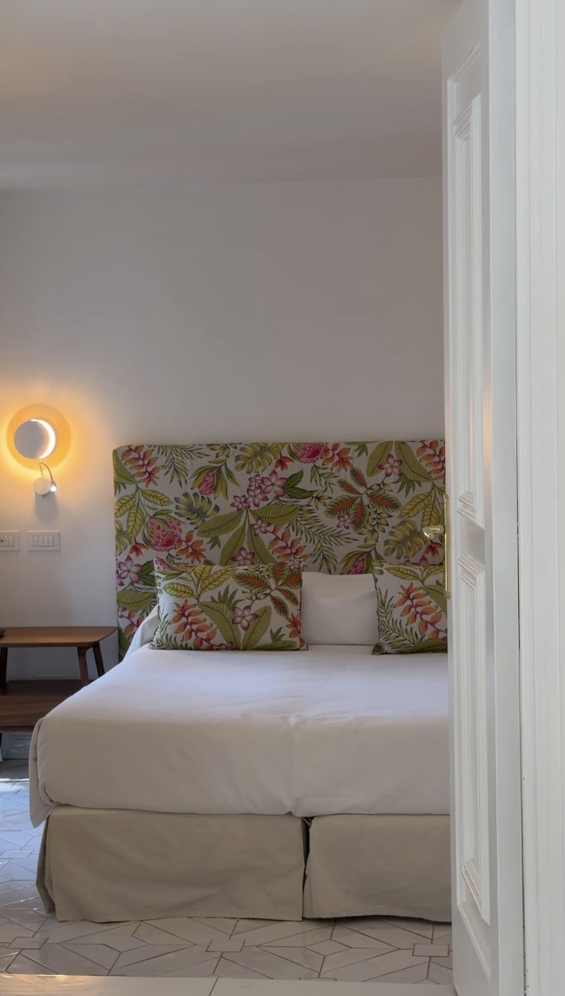 A bed with a tropical floral headboard and a crescent wall light in a Casa Marchesa room