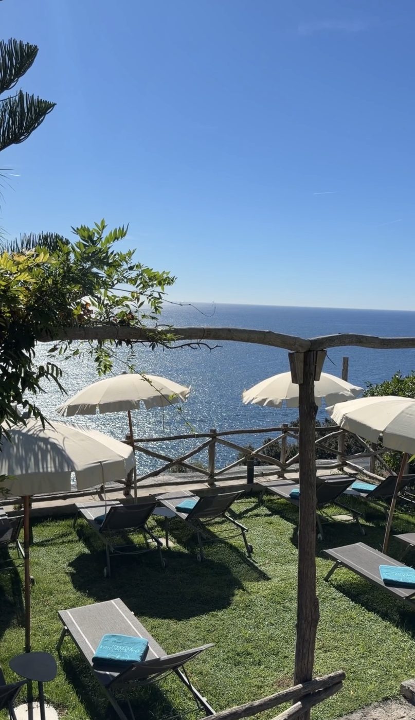 Loungers and cream umbrellas on a lawn above the sea at Casa Marchesa
