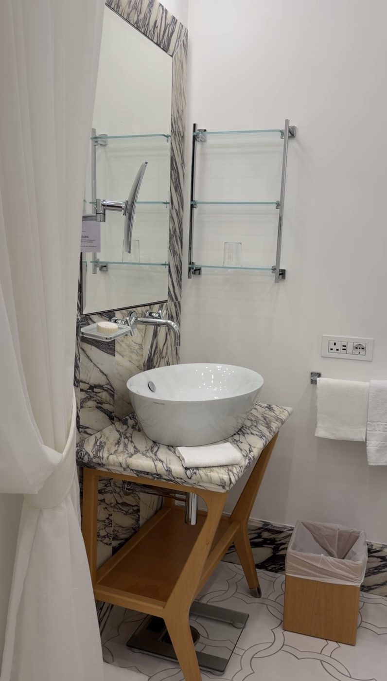A vessel sink on a veined-marble and oak stand with glass shelves at Casa Marchesa