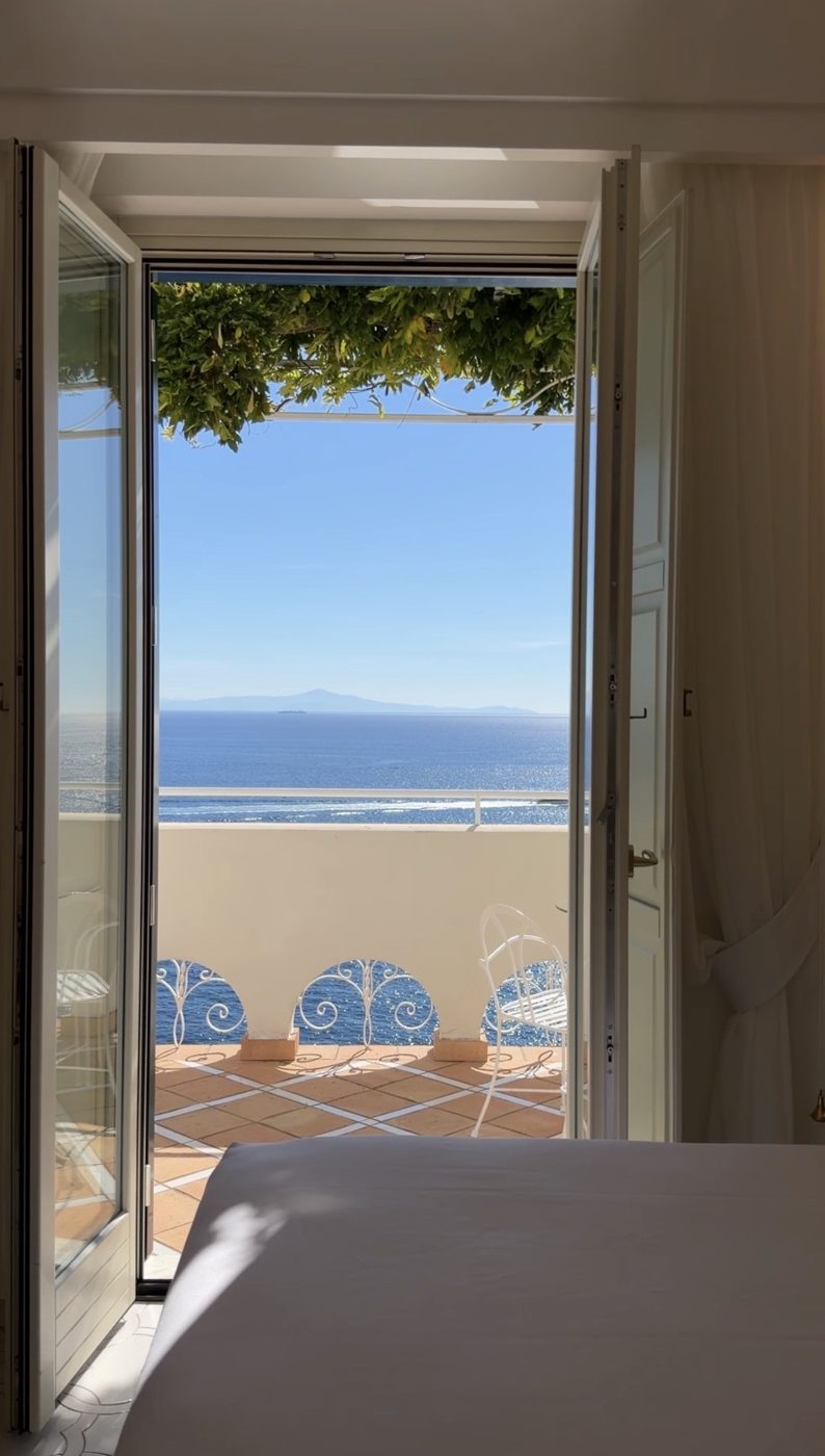 Open doors from a Casa Marchesa bedroom onto a terracotta terrace with wisteria and the open sea