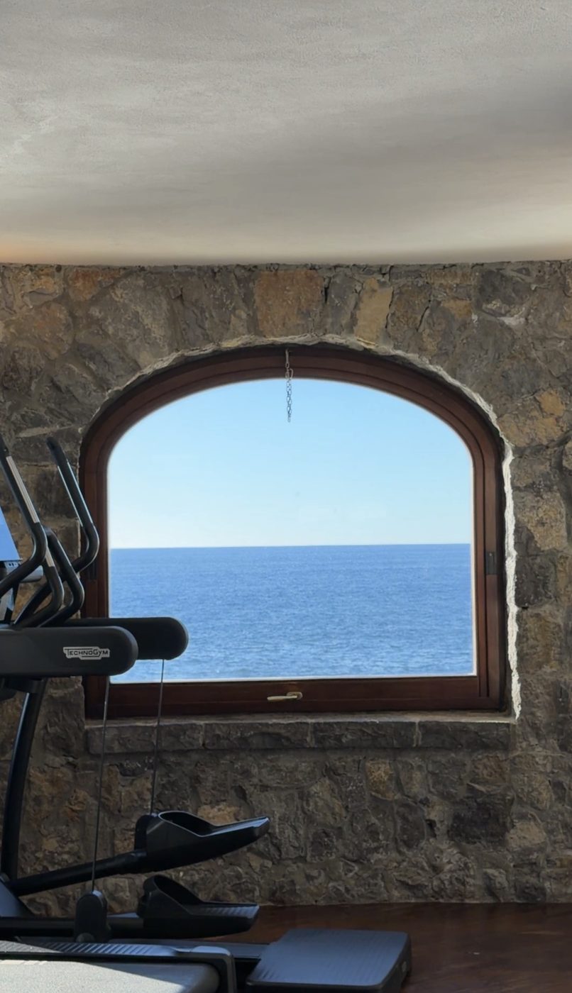 A Technogym machine in front of an arched window in a stone wall, framing nothing but open sea
