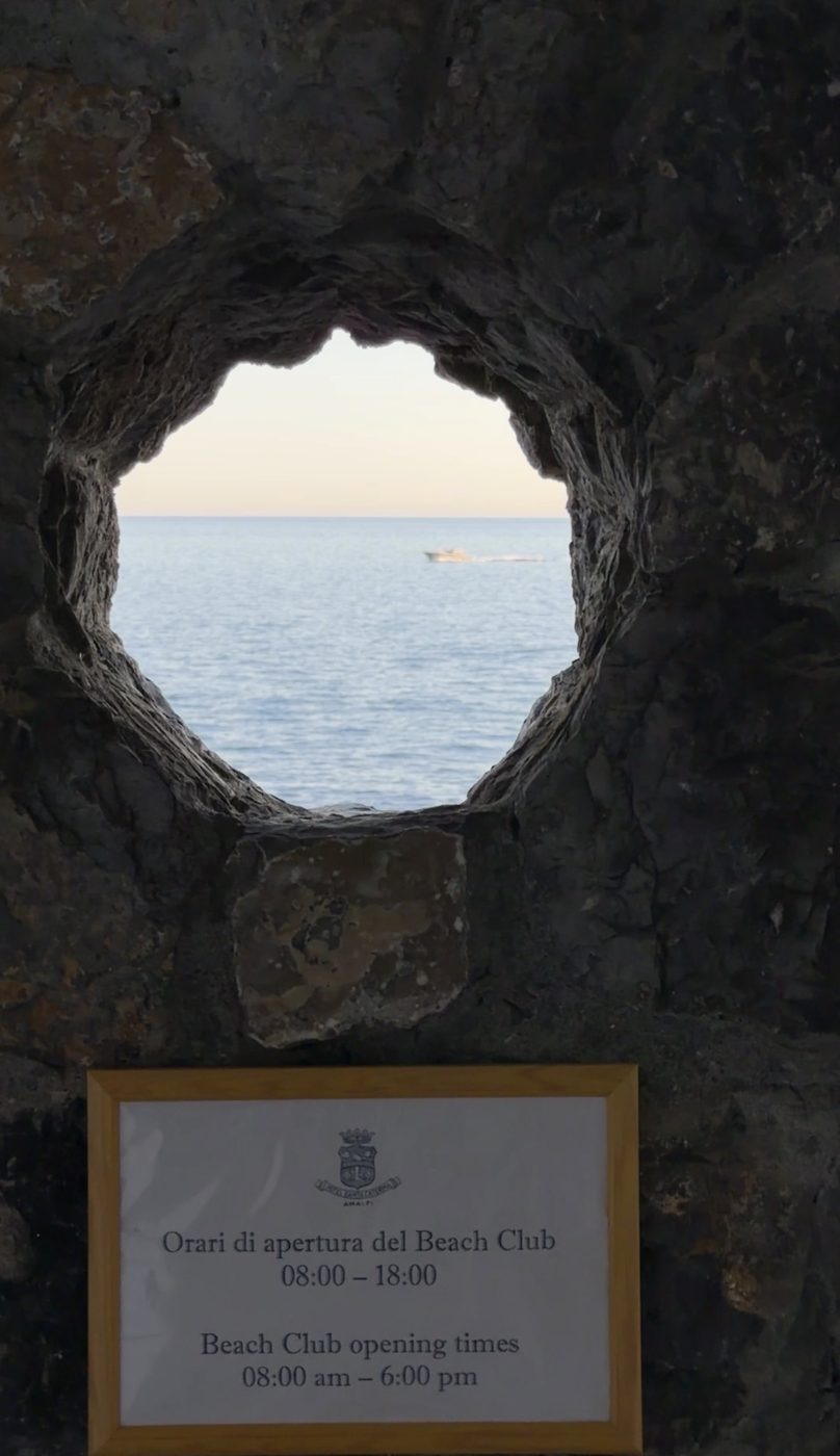 The sea and a passing boat seen through a hole in the rock above the hotel's beach club sign