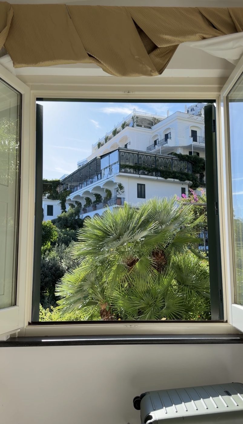 An open window framing palms and the white terraces of Hotel Santa Caterina