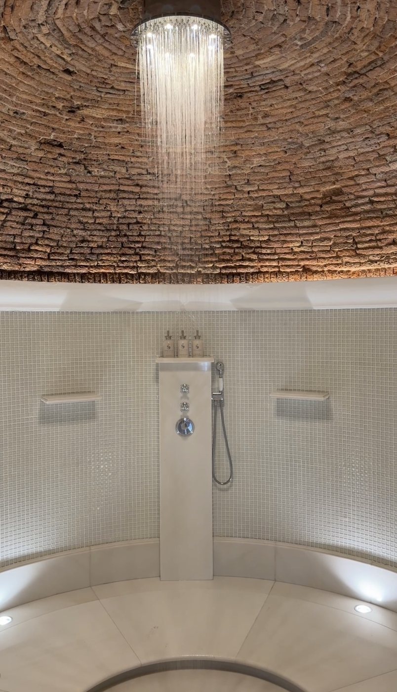 A rain shower falling from a brick-domed ceiling into a round mosaic-tiled shower at Villa Treville