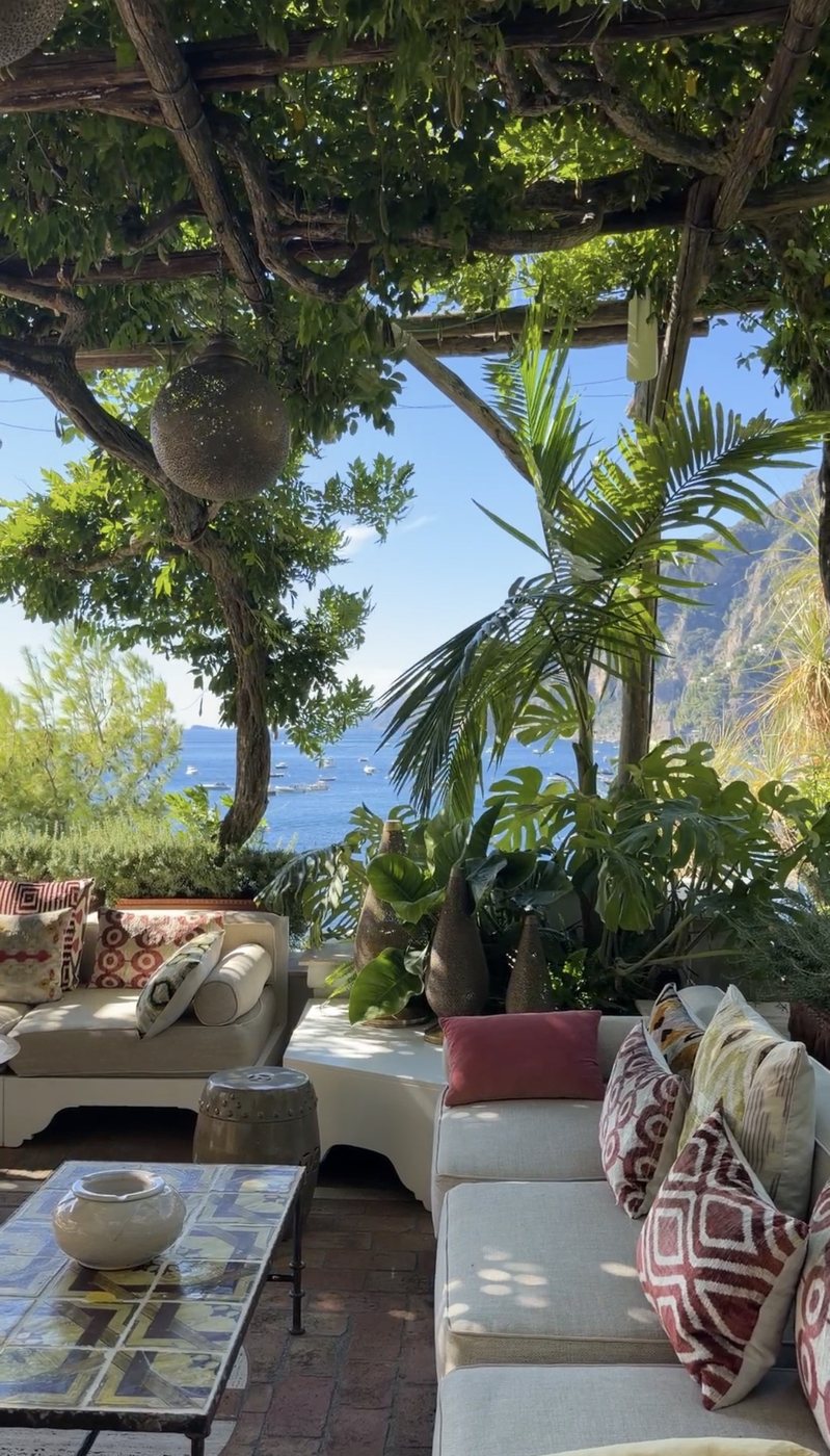 Cushioned sofas, Moroccan lanterns and palms under a wisteria pergola above the sea