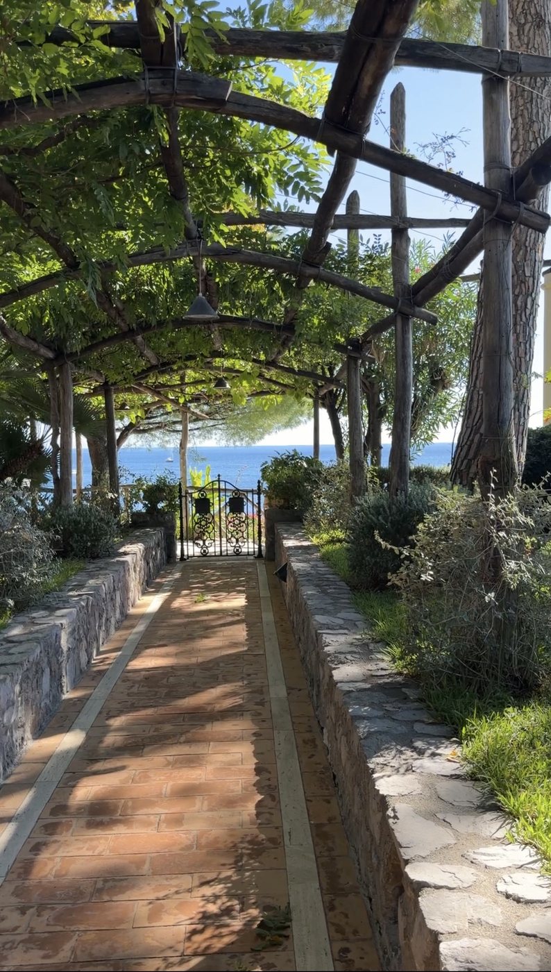 A wisteria pergola leading through the gardens to a gate above the sea at Villa Treville