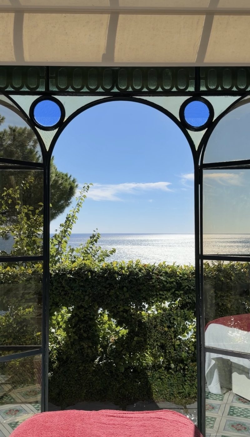 The sea through an arched iron-and-glass window in the Villa Treville spa