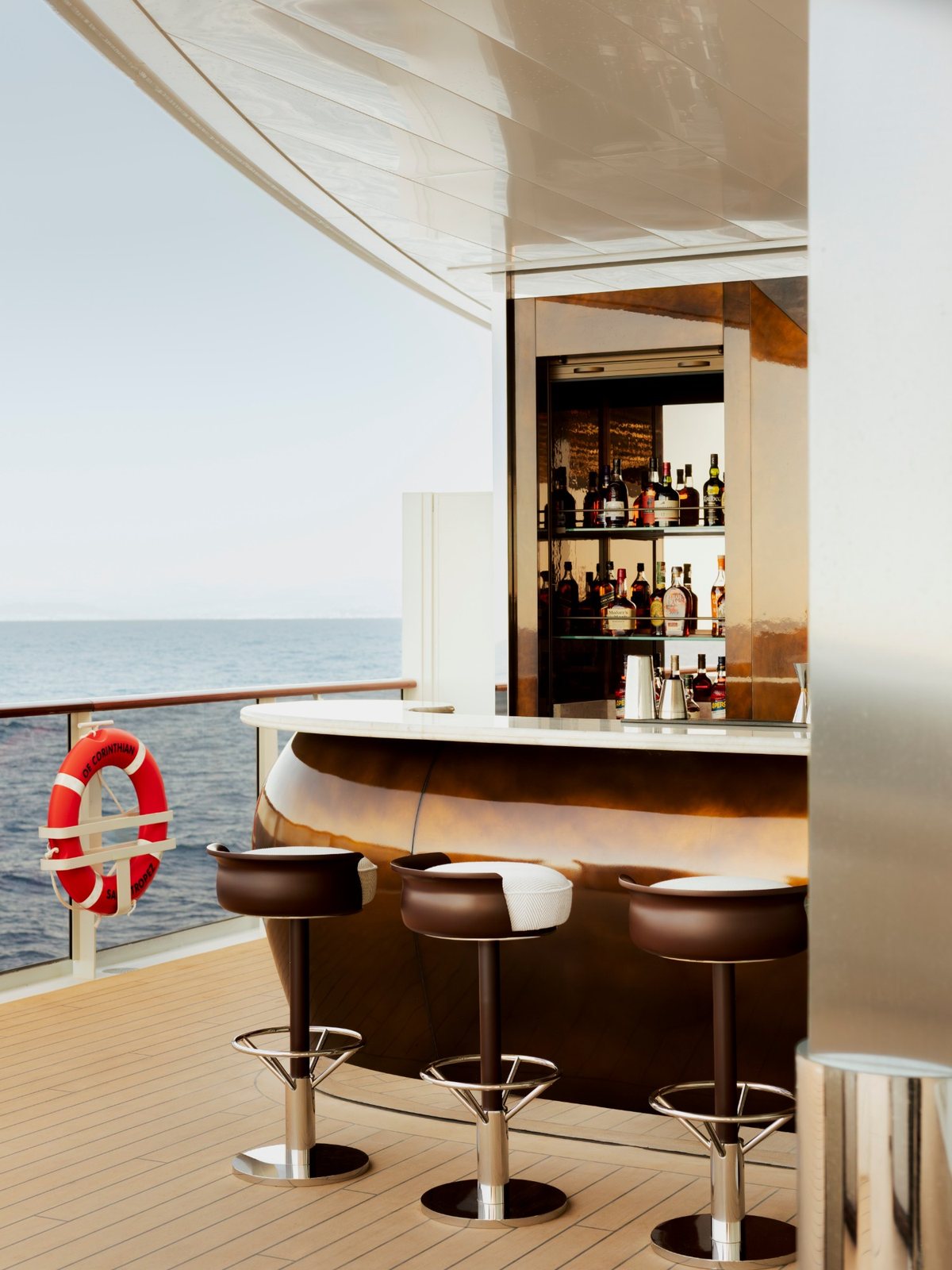 An outdoor bar on Corinthian’s teak deck, with bronze stools and the sea beyond