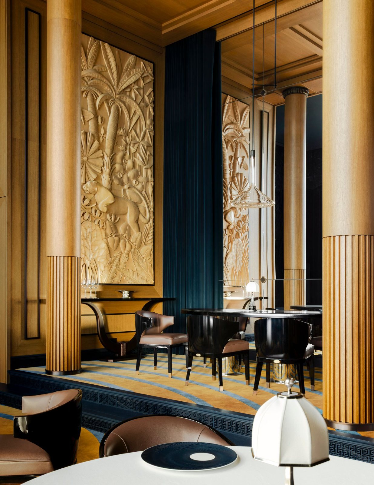 An Art Deco dining room on Corinthian, with carved wood panels, fluted columns and teal velvet