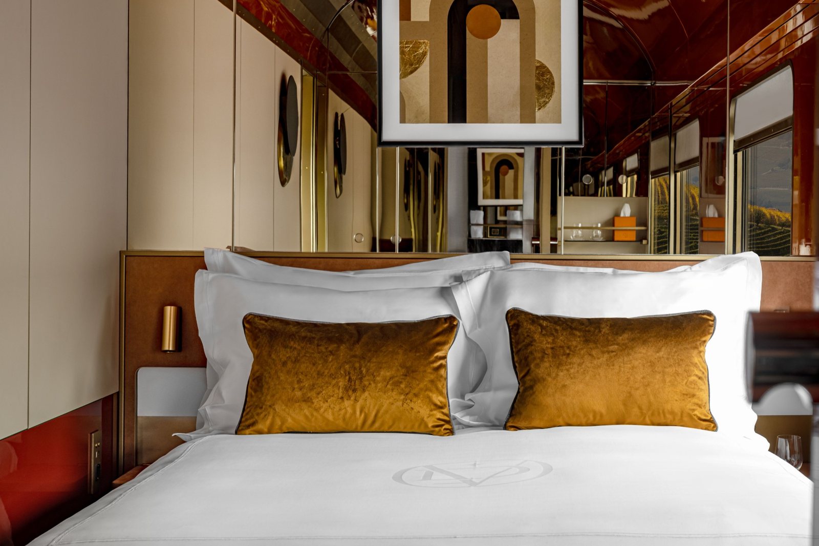 A made-up bed with gold velvet cushions and monogrammed linen in a La Dolce Vita cabin